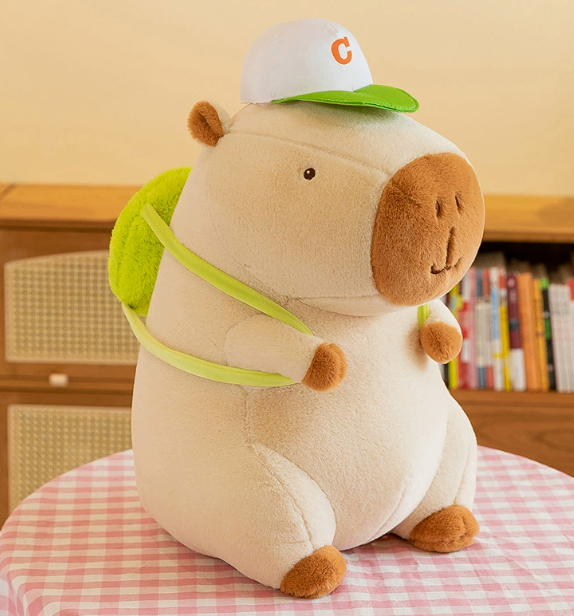 CapyCuddle capybara plush in cream with green cap and green backpack